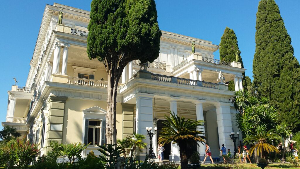 Luxurious white facade of Achilleion Palace surrounded by lush greenery in Corfu