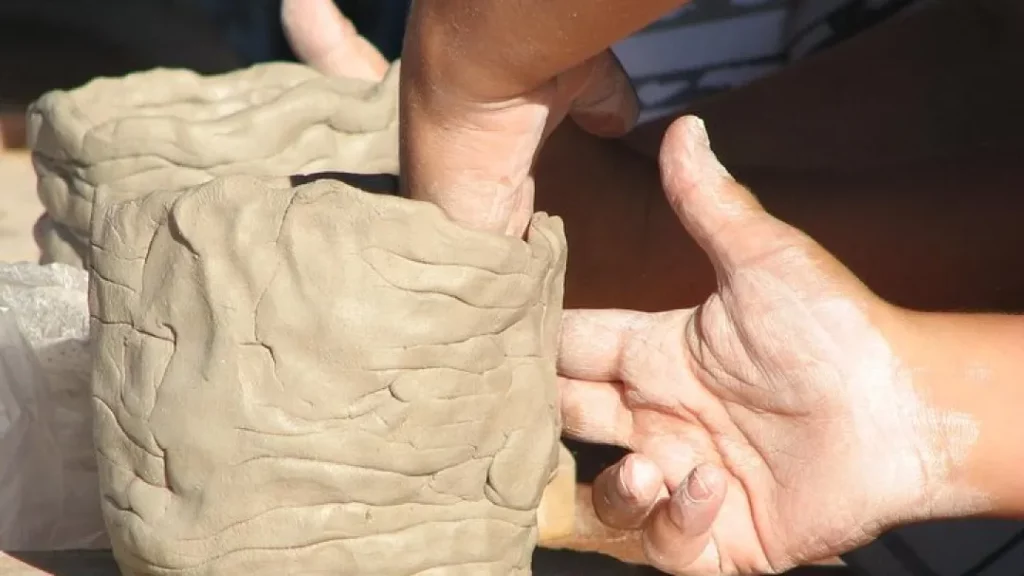 Artisan and participant shaping clay on a pottery wheel during a ceramic-making workshop in Zakynthos, Greece, surrounded by handcrafted pottery and traditional tools in a sunlit studio.